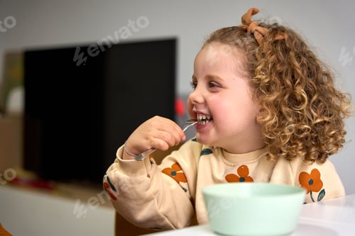 Preview: A young girl is eating a bowl of cereal while wearing a floral sweater