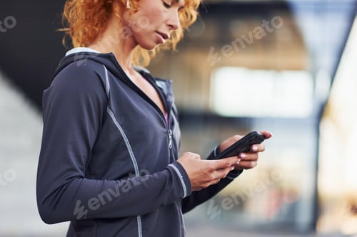 Preview: Portrait of young european redhead woman that standing with phone in hands outdoors