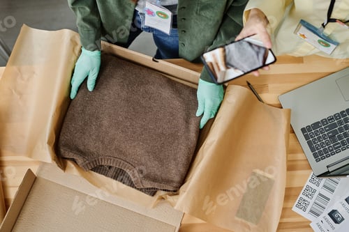 Preview: Top view of gloved hands of volunteer putting folded sweater into box