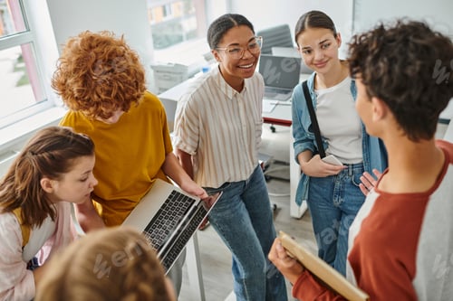 Preview: redhead boy showing laptop to classmate, african american teacher smiling near students