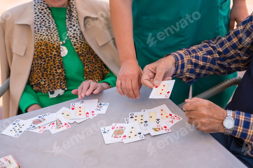 Preview: Hands of two elderly people in the garden of a nursing home or retirement home playing cards