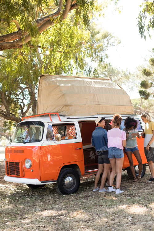 Preview: Full length of friends standing by camper van