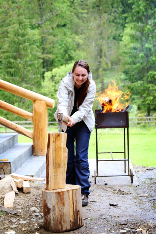 Preview: Young Woman cutting fire wood with an axe on a log
