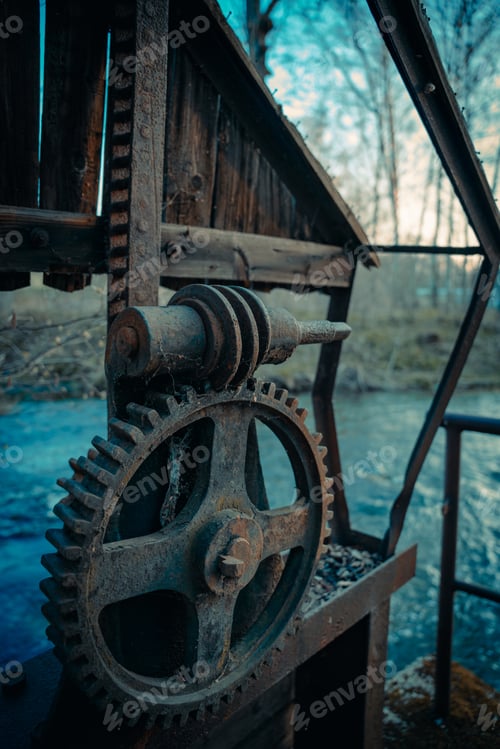 Preview: Vertical shot of an old and rustic metal gear on the side of a river