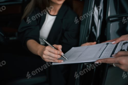 Preview: Process of buying new car, woman is signing documents while sitting in a new automobile