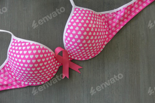 Preview: October is Breast Cancer Awareness Month. Pink Bra with pink ribbon on wooden surface.