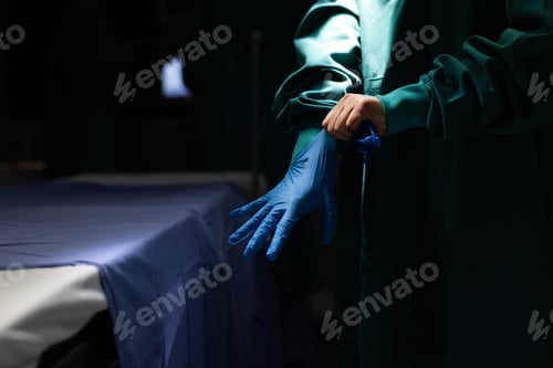Preview: Midsection of surgeon putting on glove in dark operating theatre, with copy space