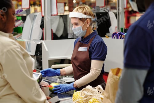 Preview: Mature cashier in uniform and protective mask, gloves and face screen