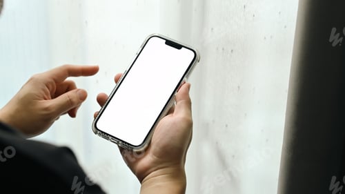 Preview: Close up view of man standing near window and using smart phone.