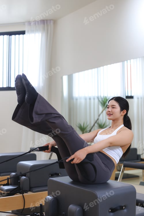 Preview: Asian woman exercising pilates on reformer chair enjoying workout