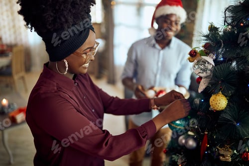 Preview: Happy African American couple decorating Christmas tree at home.