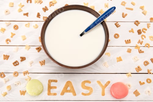 Preview: Close-up view of milk and spoon in bowl, word easy from breakfast cereal letters, macarons and