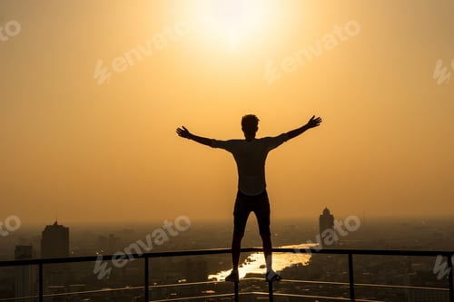 Preview: Silhouette of man standing with extend arms action over the cityscape background at sunset time