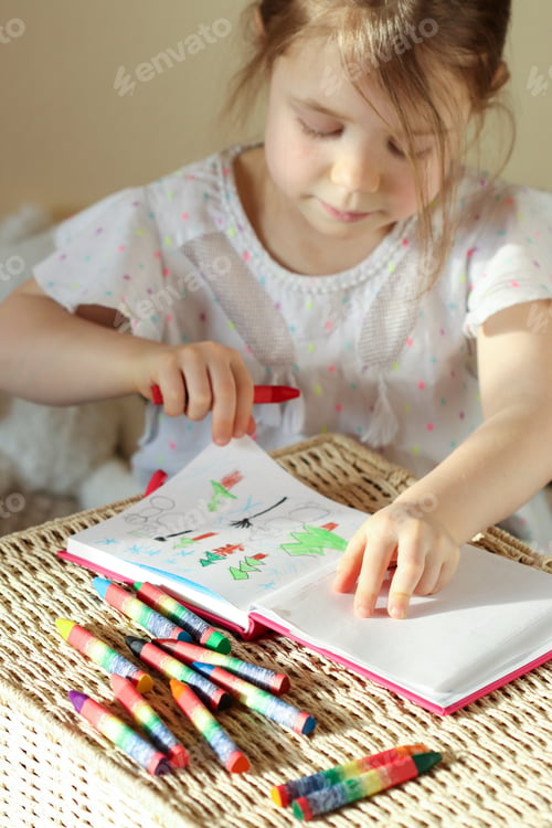 Preview: Little girl 6 years old draws with wax crayons in a sketch book