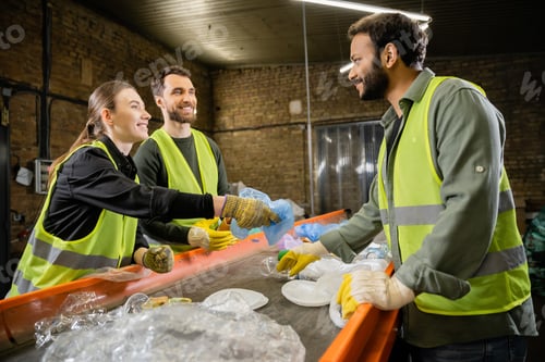 Preview: Smiling sorters in protective vests and gloves looking at indian colleague near plastic trash