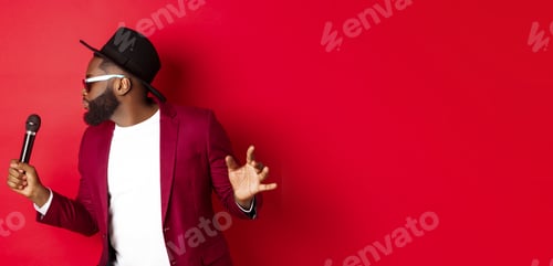 Preview: Passionate black male singer performing against red background, singing into microphone, wearing