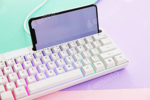 Preview: Modern computer keyboard with RGB lighting and smartphone on color background, closeup