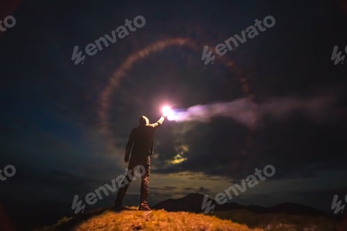 Preview: The male with a bright firework stick standing on a mountain. evening night time.
