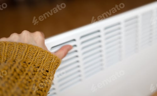 Preview: Woman warming her hand on a warm electric heater, saving energy, heating season concept