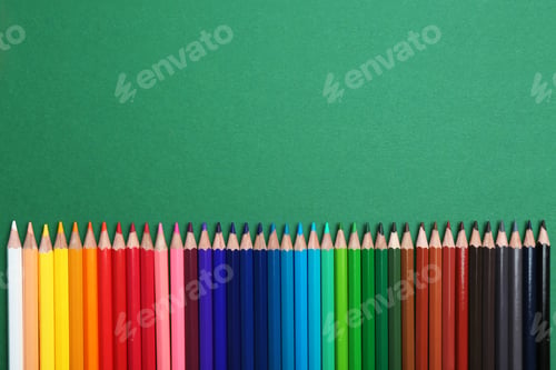 Preview: Color pencils on green background, flat lay. Space for text