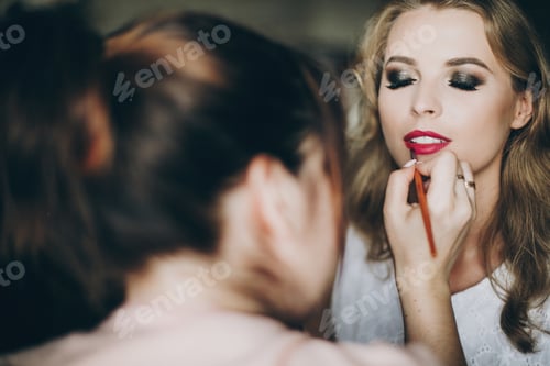 Preview: Beautiful happy bride getting her makeup done by professional make up artist
