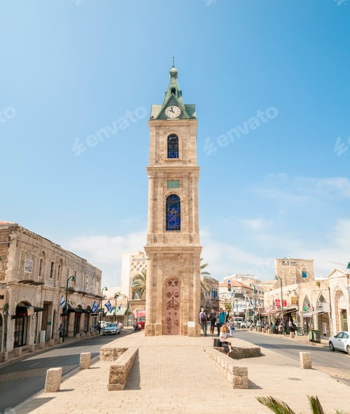 Preview: Historic clock tower standing tall under a clear blue sky in a lively town square.