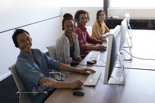 Preview: Portrait of happy young diverse executives smiling while sitting at desk with headset on in office
