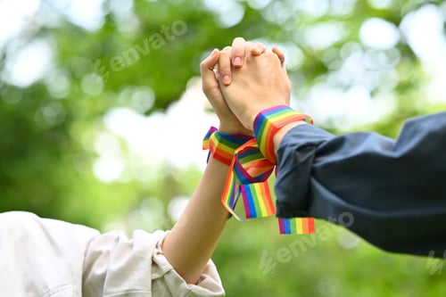 Preview: Gay couple wearing rainbow awareness wristbands holding hands.