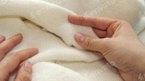 Preview: female's hand on the fabric of white plush cloth with soft nap. Clothing industry concept, slow