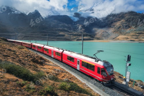 Preview: Red train is moving along railway in swiss alps mountain. Autumn