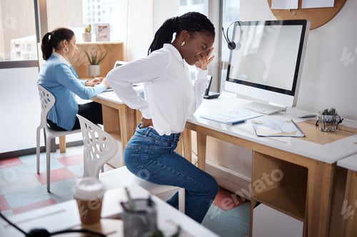 Preview: Shot of a young businesswoman experiencing back pain while working at her desk in a modern office
