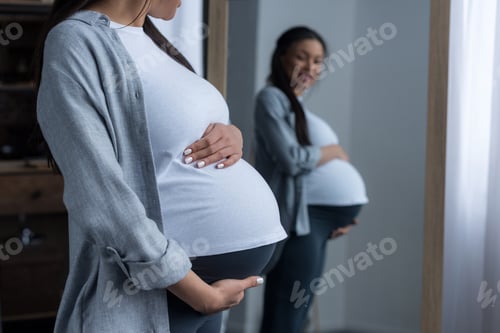 Preview: african american pregnant woman looking at her belly in mirror