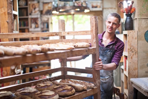 Preview: Portrait of young male baker with shelves of fresh bread