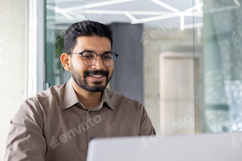 Preview: Indian businessman working happily on laptop in office