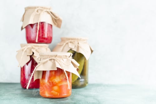 Preview: Preserved vegetables in glass jars on a light green background with copy space.