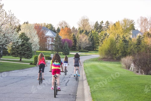 Four 4 teen girls biking in the suburbs through a neighborhood with trees changing colors