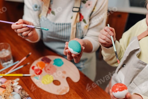 Preview: Grandmother and granddaughter painting easter eggs together at home