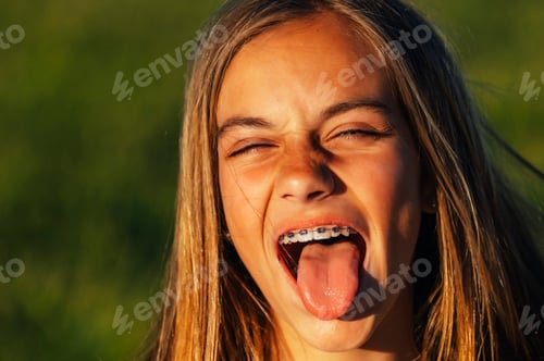 Preview: Portrait of a beautiful young blonde woman showing her tongue and a bracket in her teeth.