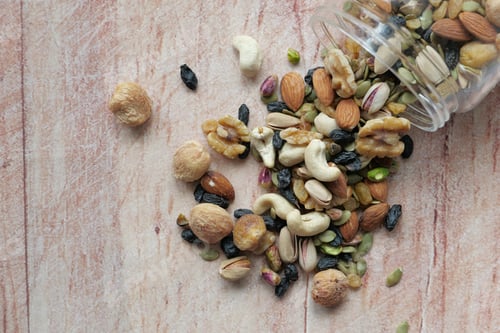 Preview: Nuts and seeds spilled from a glass jar onto rustic wood, creating a delightful scene