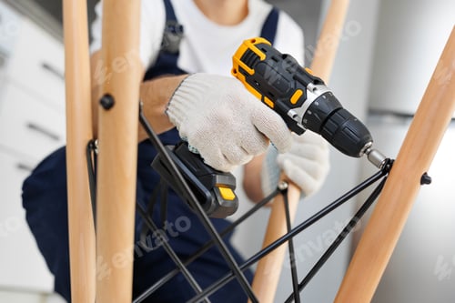 Preview: Man in a blue jumpsuit is using an electric drill to assemble a table.