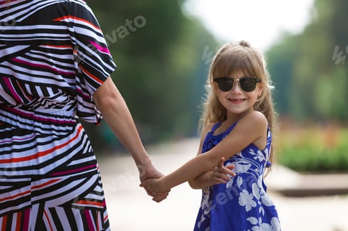 Preview: Back view of young blond long-haired attractive woman and small child girl holding hands outdoors.