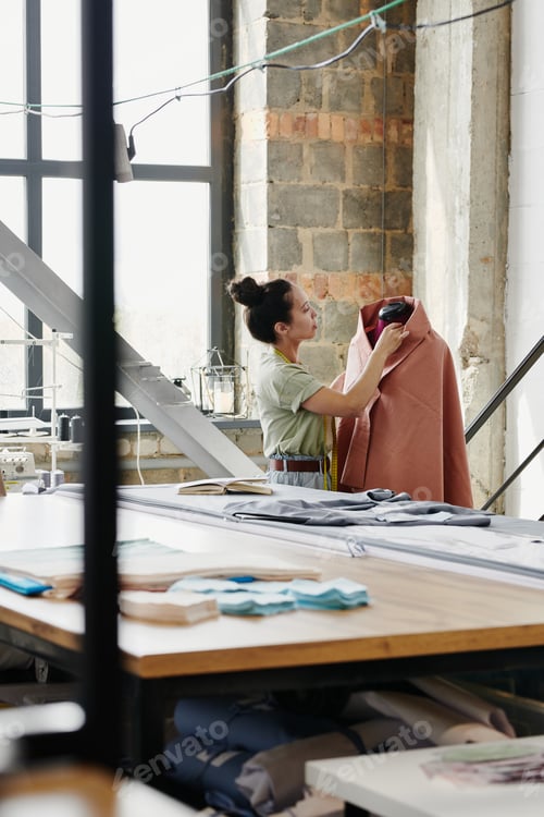 Preview: Female worker of modern fashion design studio sewing clothing item on dummy