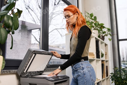 Preview: Young woman with red hair engaged in office tasks at a modern workspace