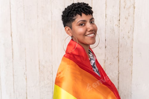 Preview: Young person smiling and wrapped in rainbow flag celebrating lgbtq+ pride