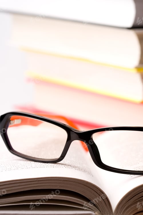 Preview: Reading Glasses on Book Stacked on White Background