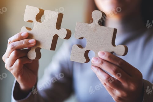 Preview: Closeup image of a woman holding and putting a piece of wooden jigsaw puzzle together