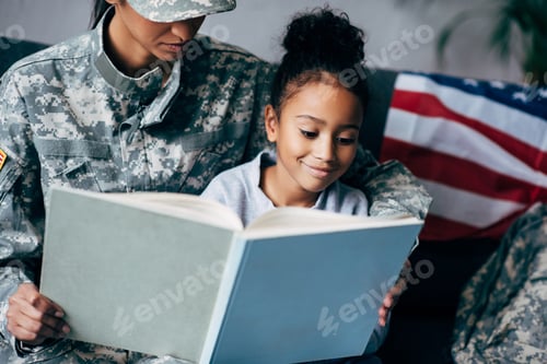 Preview: african american daughter and mother in military uniform reading book together at home