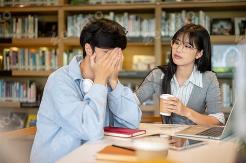 Preview: Glasses asian woman student comforting a crying man or sad friend while sitting at library's table.