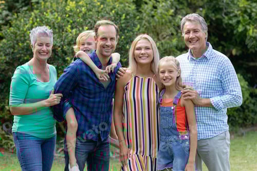 Preview: Portrait of caucasian parents, grandparents and grandchildren standing in garden smiling to camera
