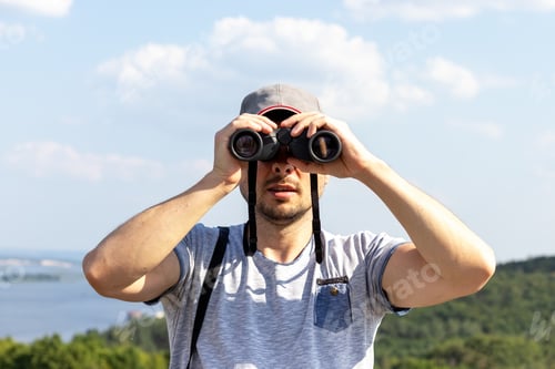 Preview: Man looking at camera through binoculars against scenic view